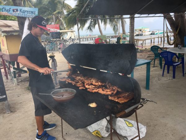 Best Things to Do in Caye Caulker featured by top US travel blog, The Common Traveler: man grilling food on shack on beach