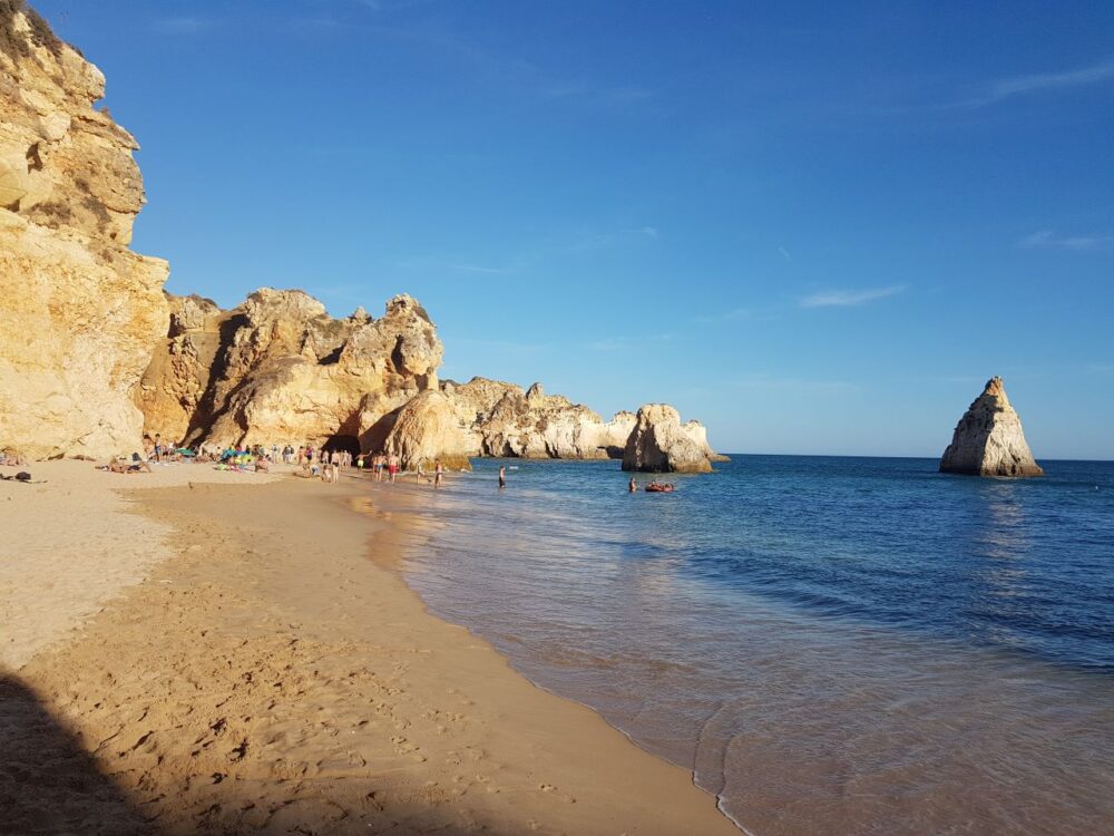 image: people on beach at foot of mountains in the Algarve, Portugal |Things to do in Portugal by popular US international blog, The Common Traveler: image of The Algarve.