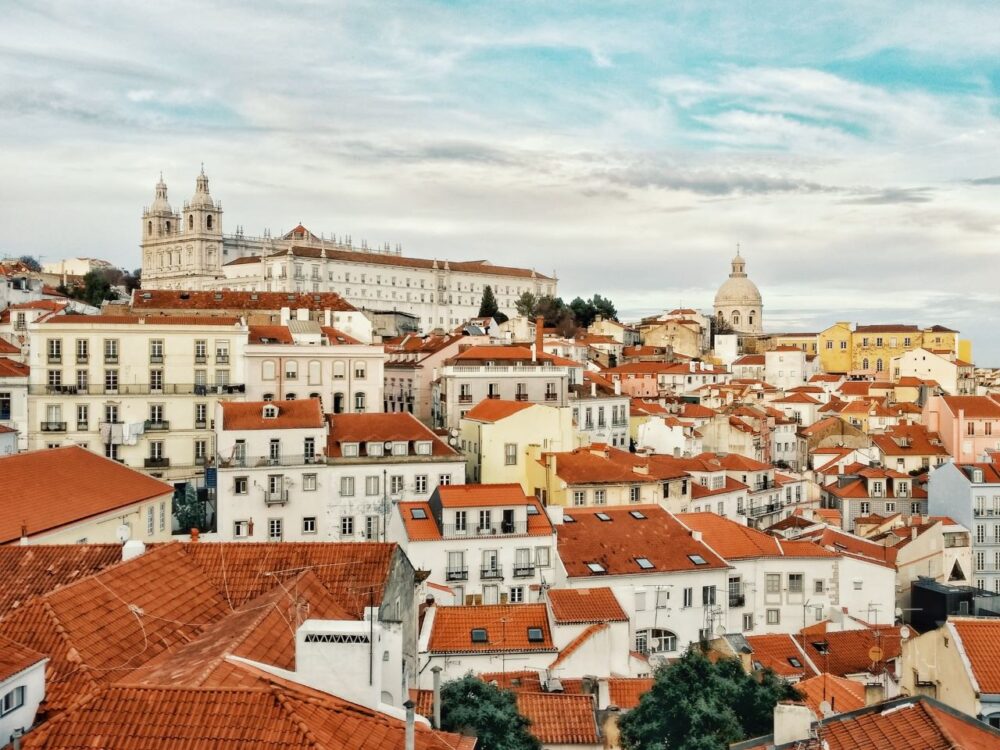 image: red rooftops over white buildings and Alfama church in Lisbon, Portugal |Things to do in Portugal by popular US international blog, The Common Traveler: image of Lisbon Portugal. 