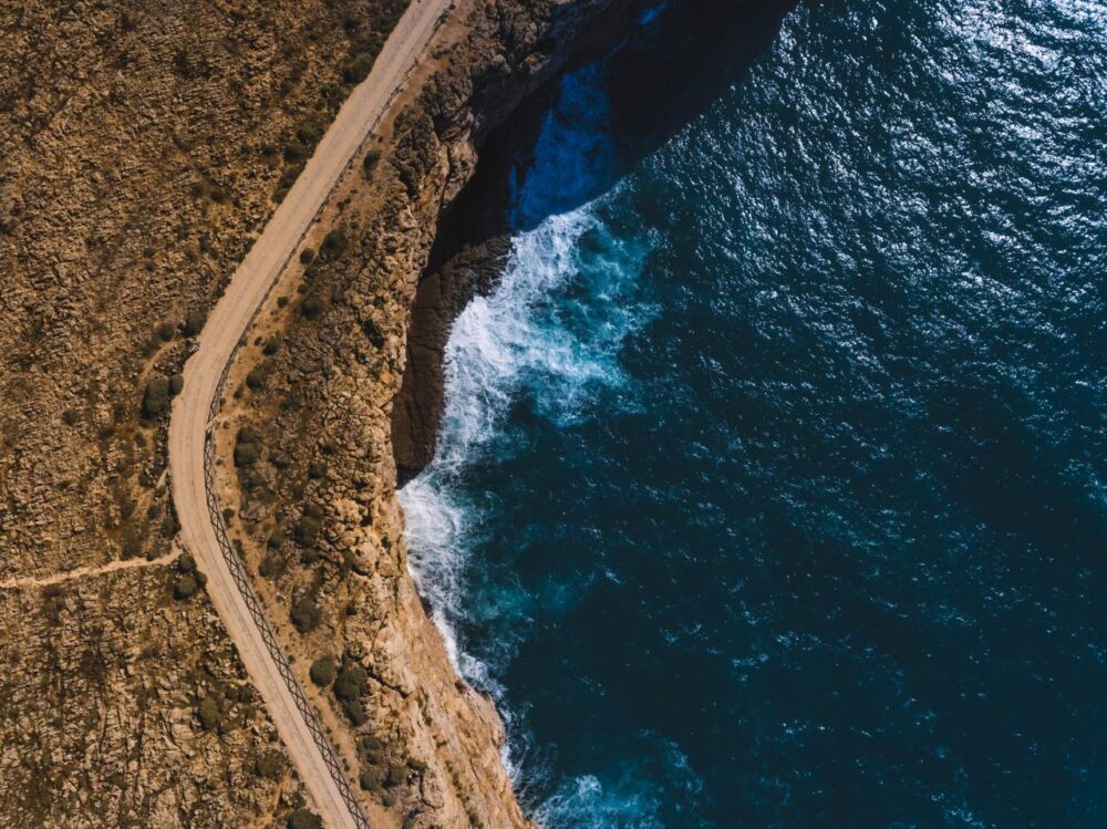 image: aerial shot of road by Atlantic ocean in Sagres, Portugal |Things to do in Portugal by popular US international blog, The Common Traveler: image of the Atlantic ocean in Sagres Portugal.  