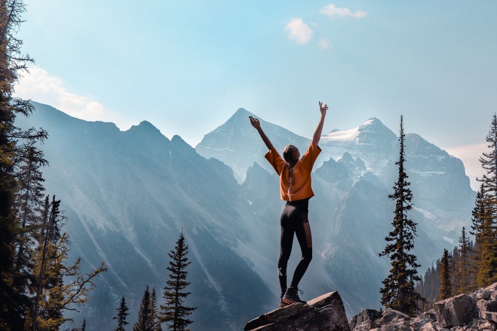 Solo Hiking Safety | The Common Traveler | image: woman on Canadian mountains. | Solo Hiking by popular US travel blog, The Common Traveler: image of a woman standing on a boulder in the mountains and outstretching her arms to the sky. 