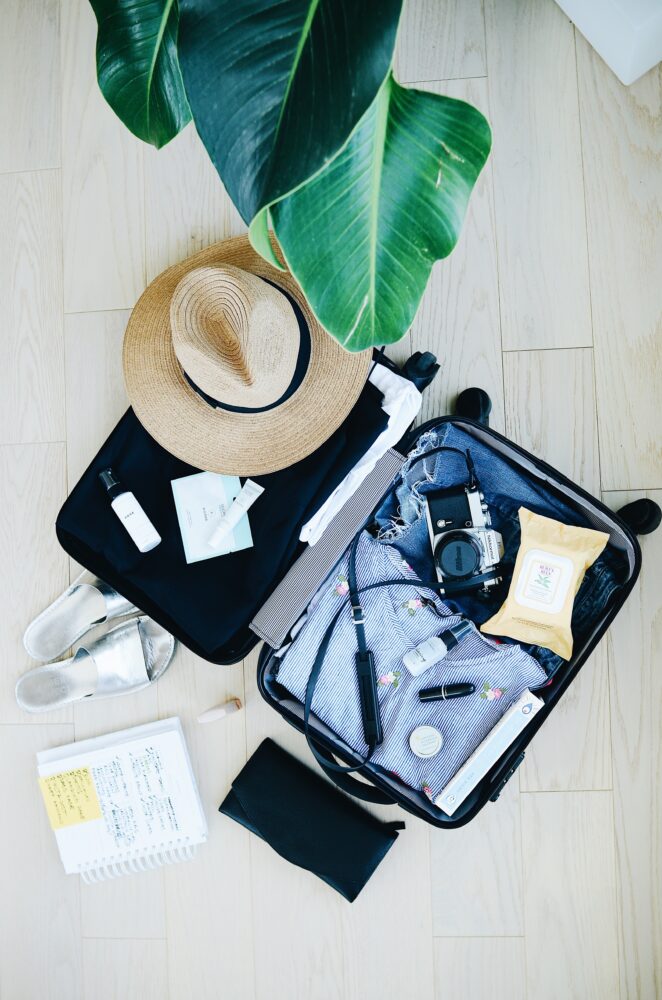 open suitcase being packed | Costa Rica Packing List: image of a open suitcase filled with clothing, straw hat, camera, silver slide sandals, personal hygiene products, and makeup. 