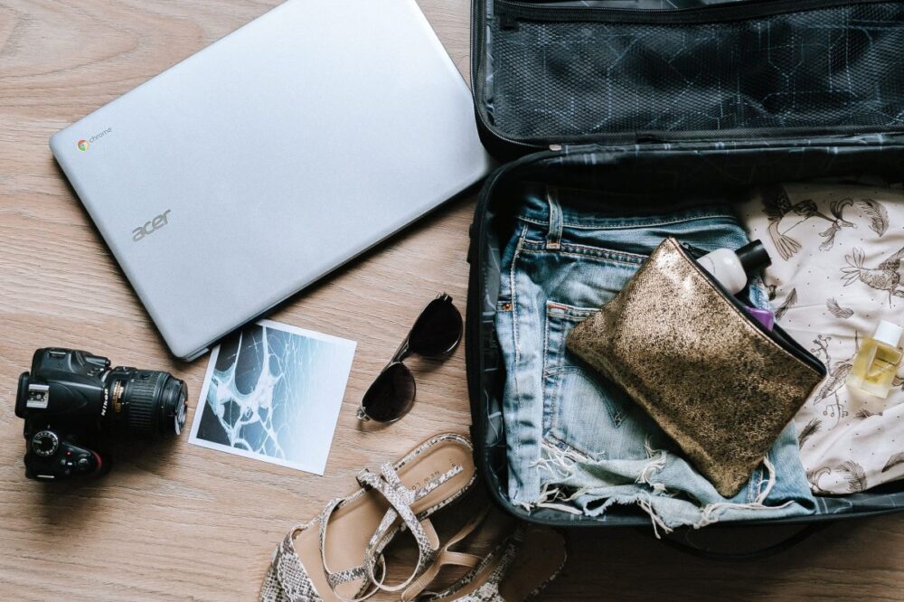 open suitcase being packed | Costa Rica Packing List: image of a open suitcase filled with clothing, sunglasses, snake print sandals, DSLR camera, and laptop. 