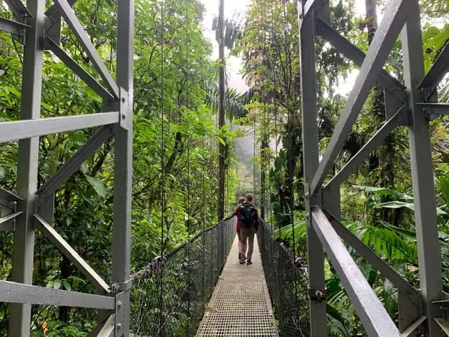 Arenal Springs Resort review featured by top international travel blogger, The Common Traveler | image: couple walking on metal hanging bridge in La Fortuna Costa Rica
