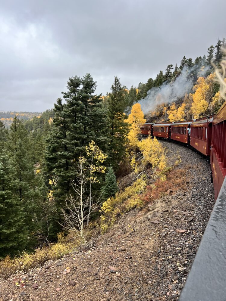 Best Scenic Steam Train Rides in America | The Common Traveler | image: red steam train going around curve with pine and yellow trees